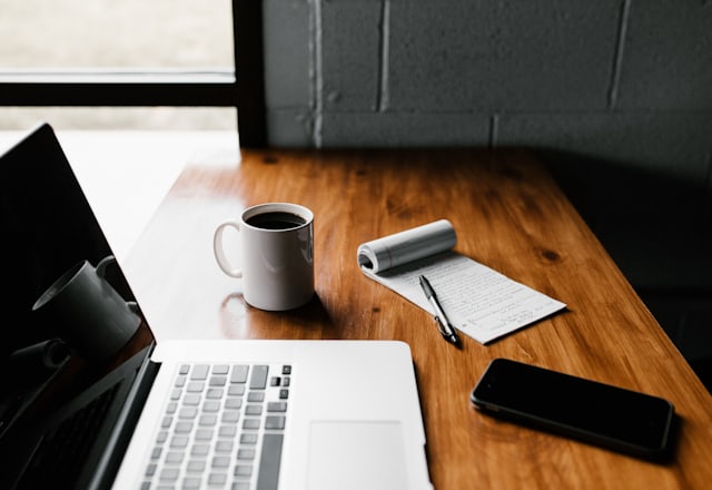 A laptop, a mug of coffee and handwritten notes on a wooden desk