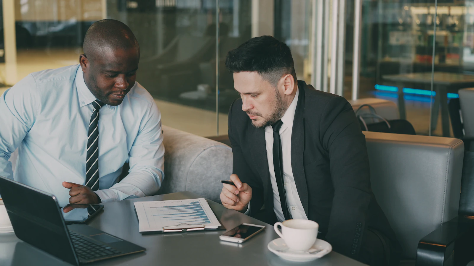 Two colleagues reviewing a printed report together at a café table, a laptop open beside them.