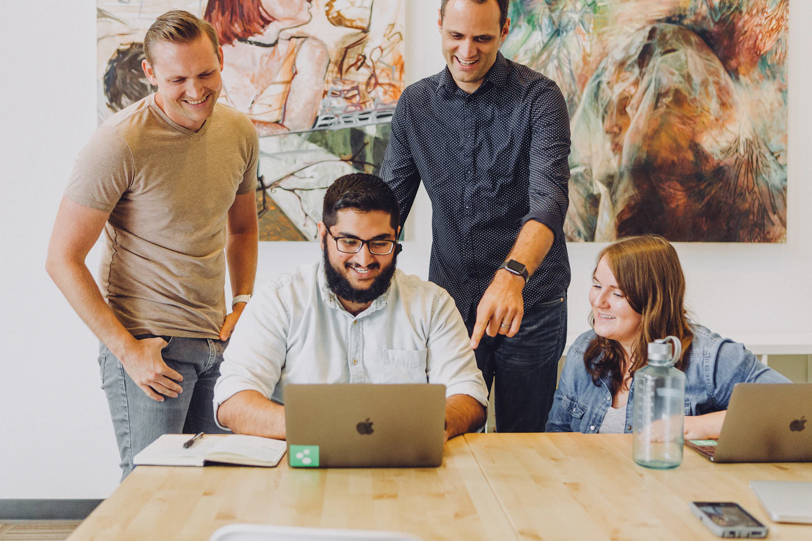 A small team gathered around one laptop, smiling at what is on the screen.